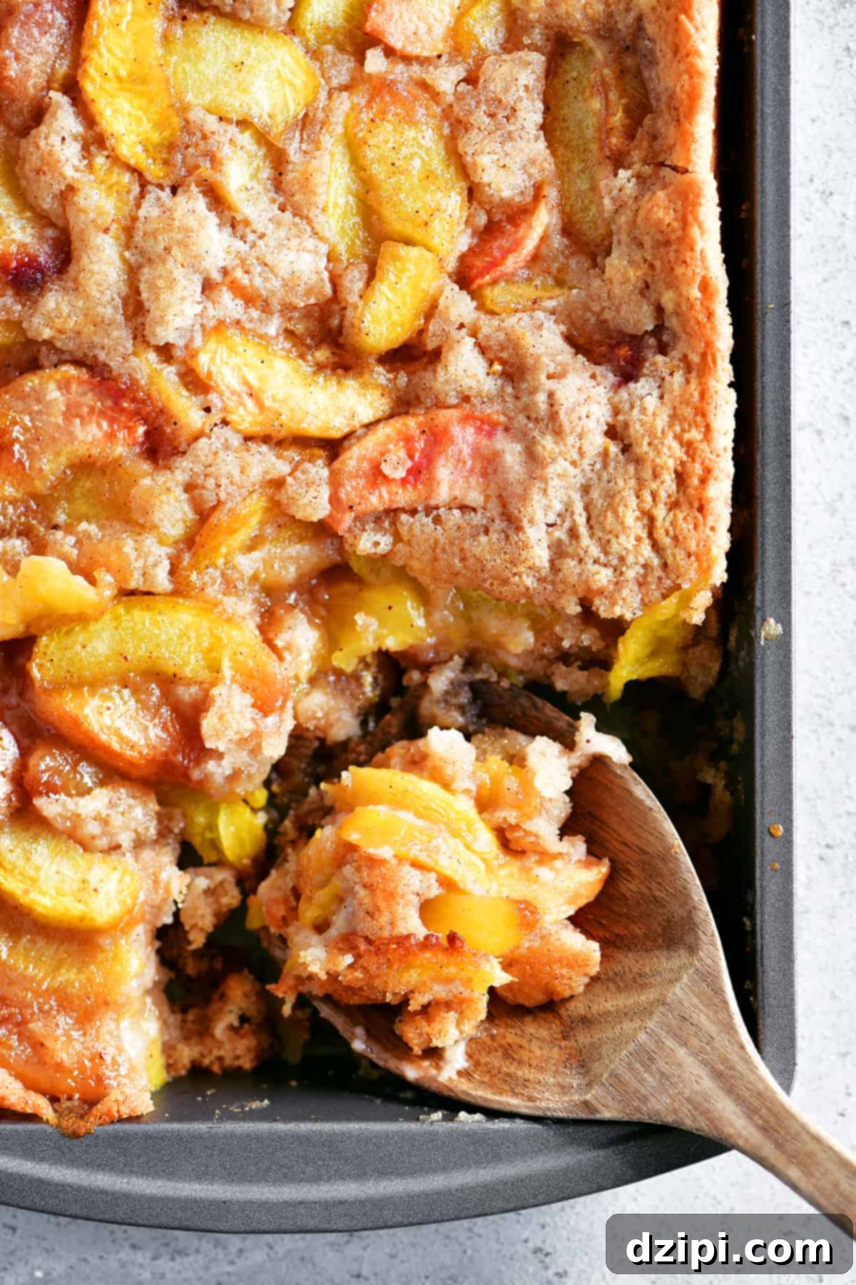 A freshly baked pan of peach cobbler, made effortlessly with Bisquick, with a portion scooped out by a wooden spoon, showcasing its golden crust and juicy fruit filling.