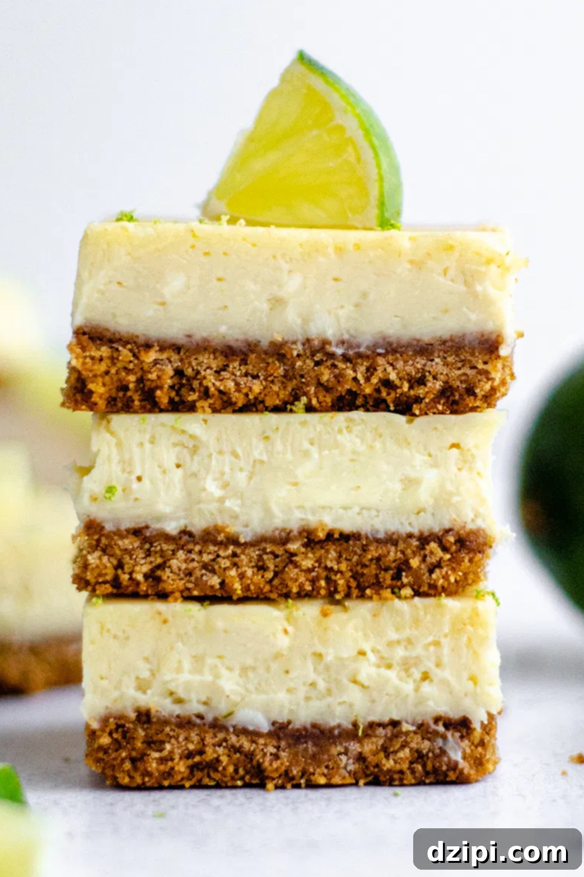 Three zesty Key Lime Pie Bars, neatly stacked, with the top bar elegantly garnished with a fresh lime slice on a light background.