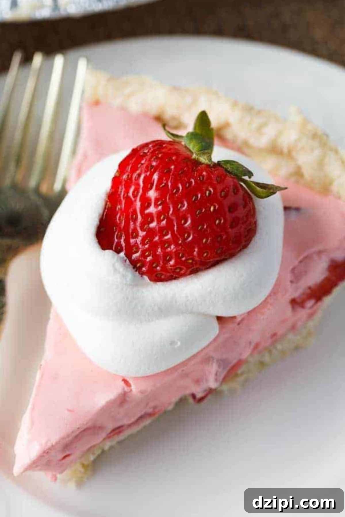 A tempting slice of pink strawberry cream pie, garnished with a swirl of whipped cream and a whole fresh strawberry, presented on a white plate.