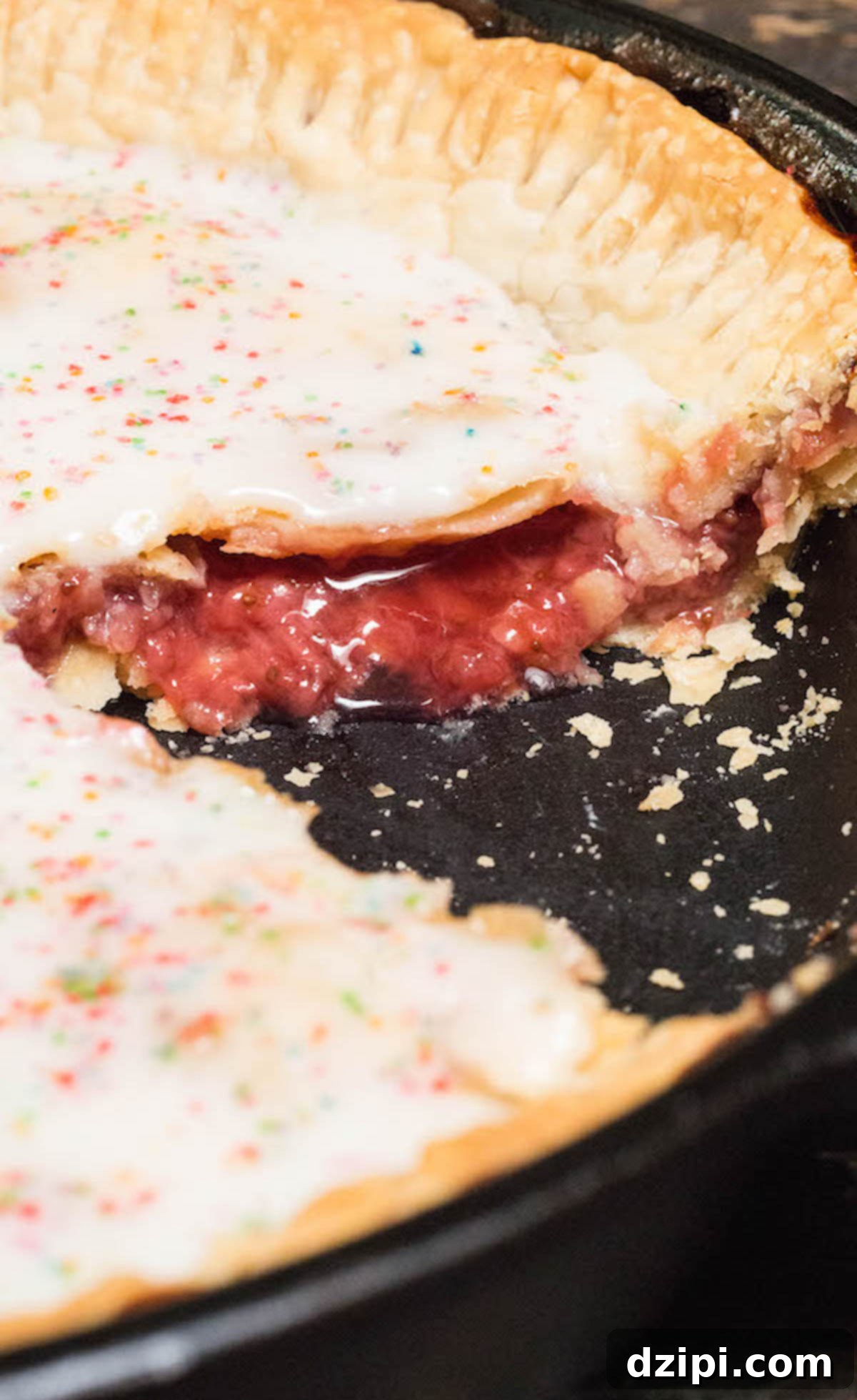 A cast iron skillet holds a glistening strawberry pie, artfully glazed to resemble a giant Pop-Tart. A slice has been removed, revealing the delicious strawberry filling within.