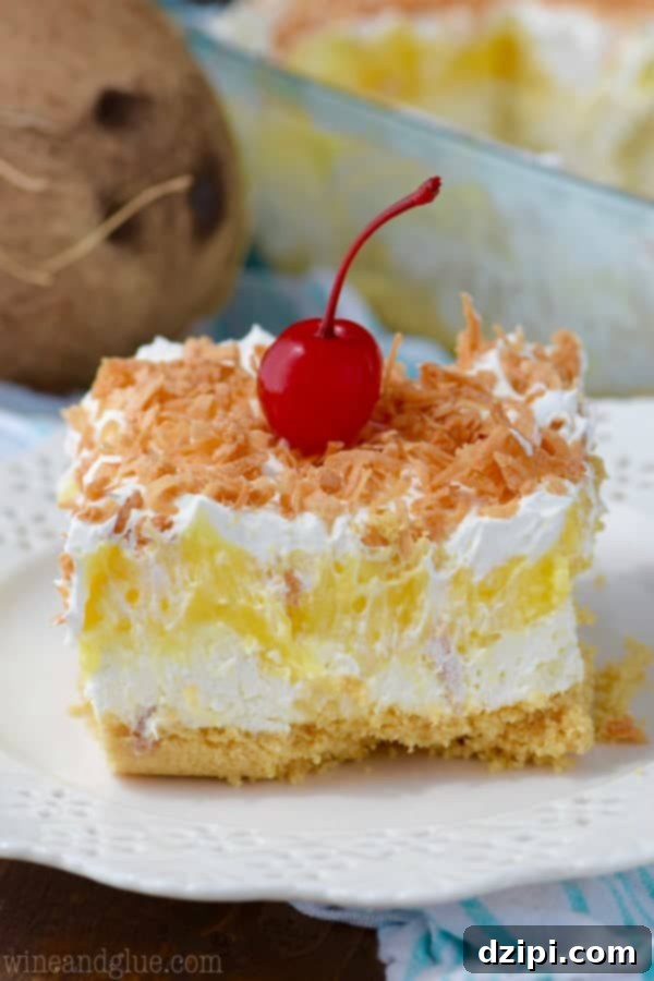 A perfectly cut square of Pina Colada Lush, showcasing its distinct layers of golden Oreo crust, pineapple, cool whip, and toasted coconut, on a white serving plate.