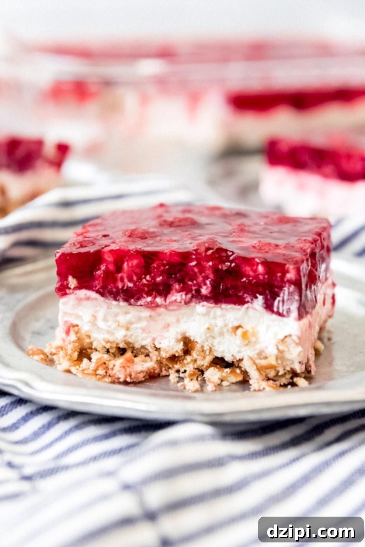 A perfectly portioned square of Raspberry Pretzel Salad, showcasing its distinct layers of crunchy pretzel crust, creamy filling, and vibrant raspberry jello top, served on a plate.