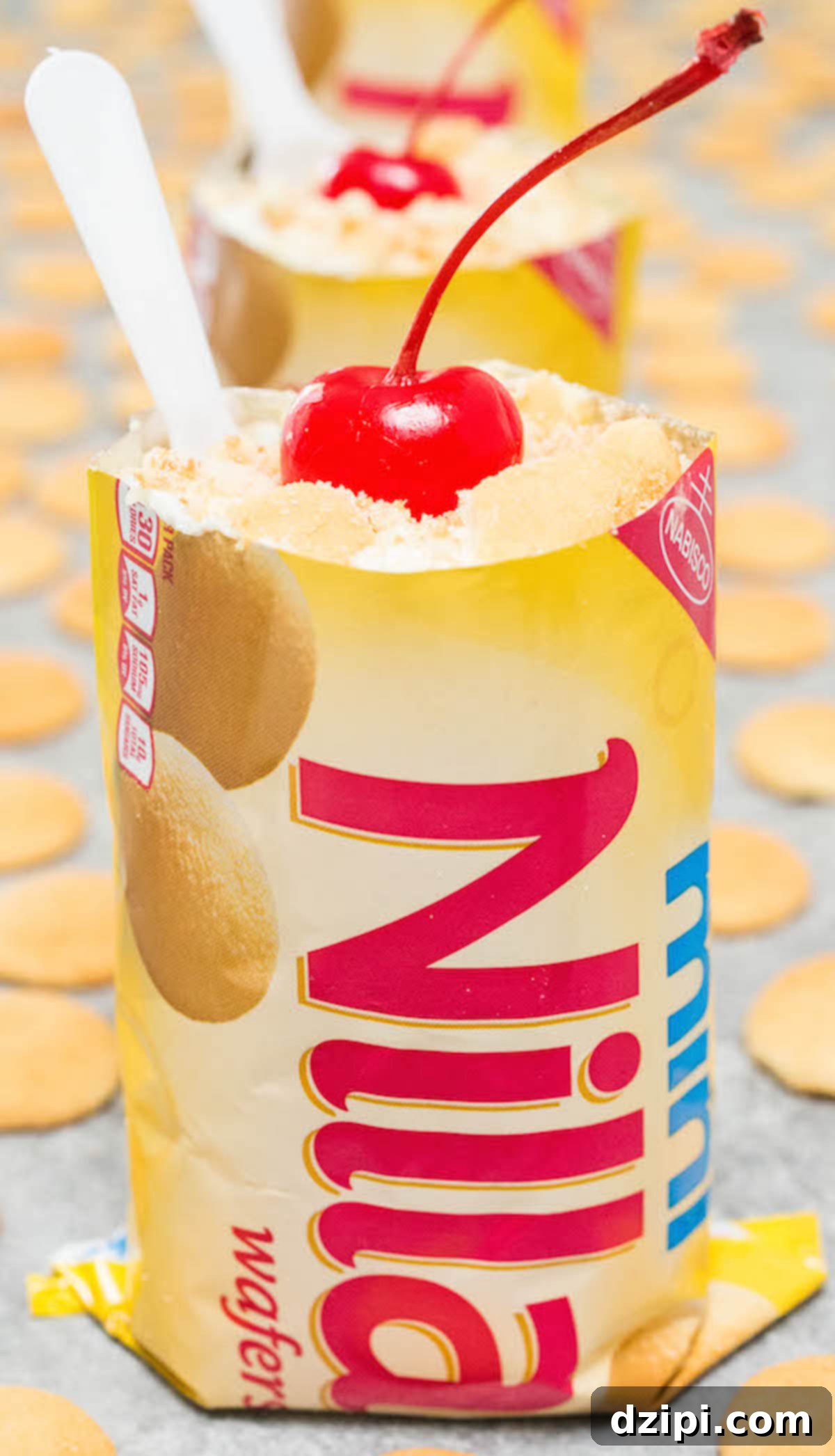 A mini Nilla Wafer bag filled with creamy banana pudding, topped with a bright maraschino cherry and a small plastic spoon, showcasing a portable dessert.