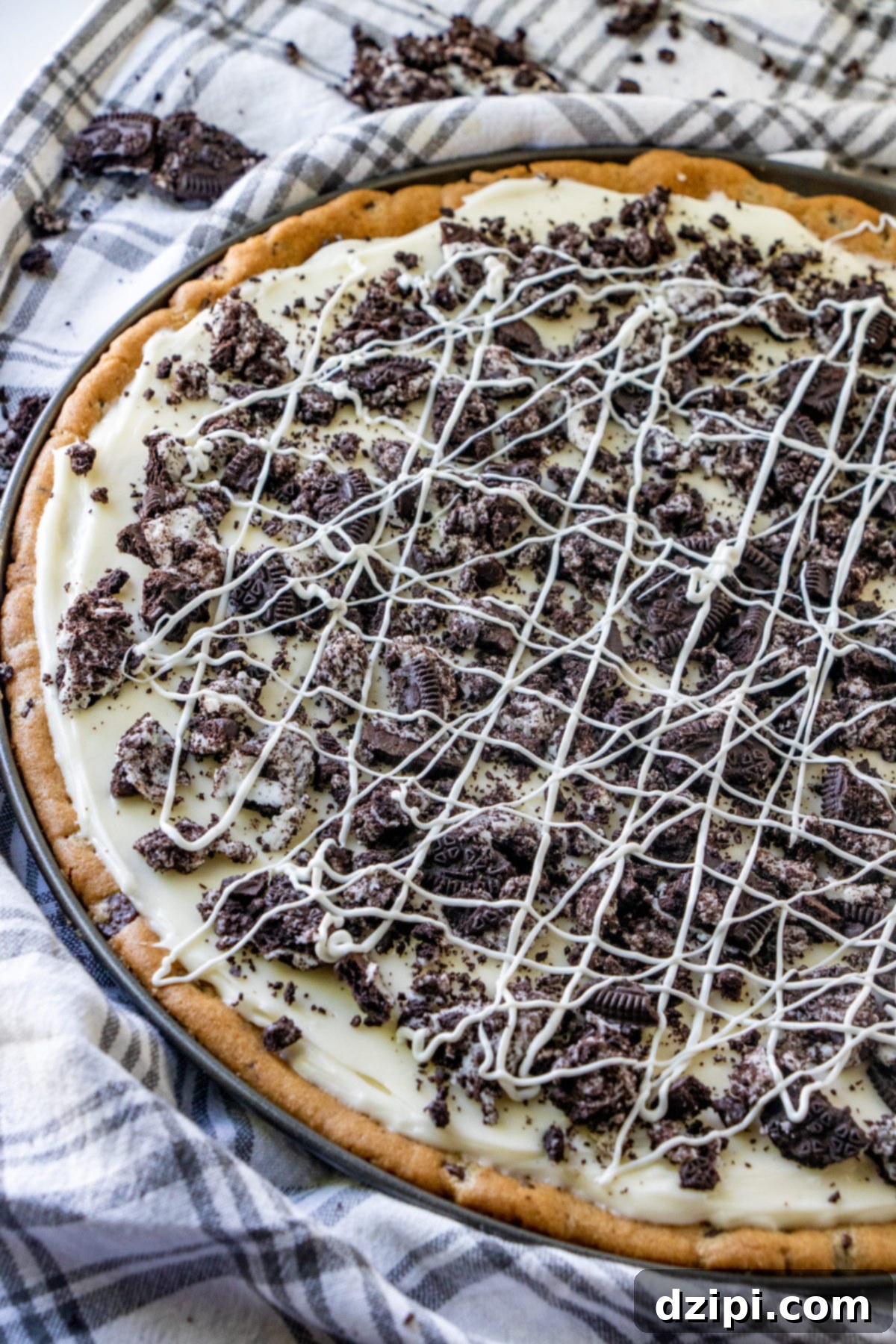 A decadent cookies and cream dessert pizza featuring a chocolate chip cookie crust, a creamy white 'sauce', and generous toppings of crushed Oreos.