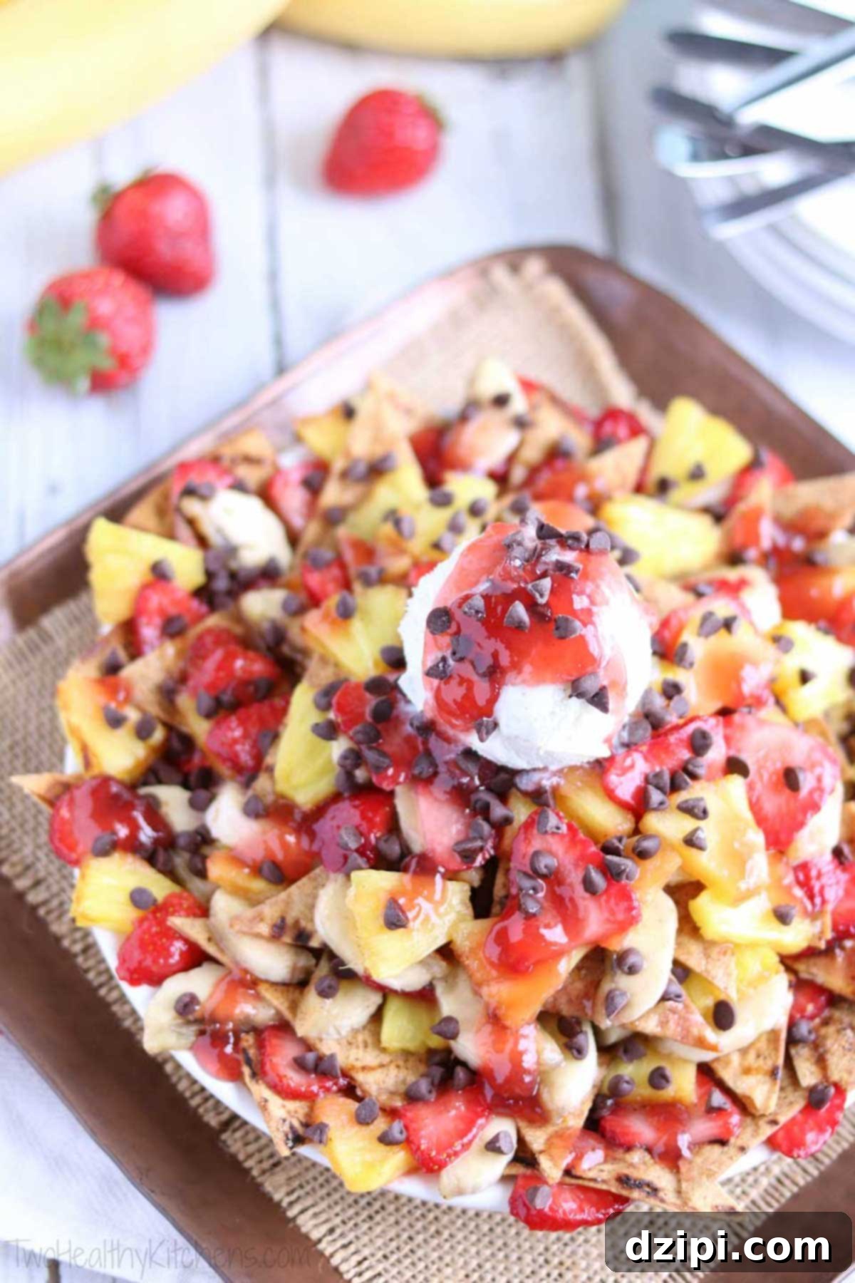 An overhead view of a tray of dessert nachos, laden with grilled strawberries, grilled bananas, chocolate chips, and crowned with a scoop of vanilla ice cream.