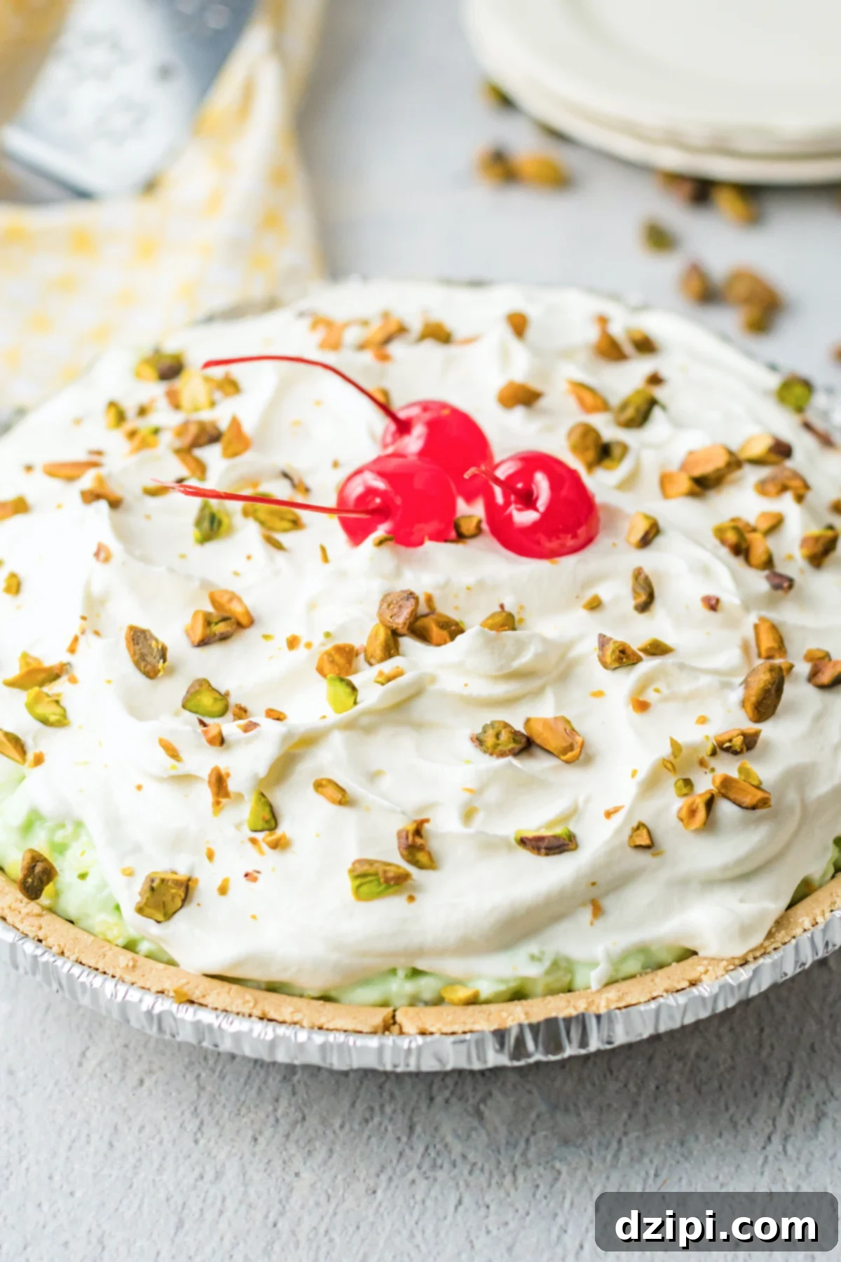 An uncut pistachio pie, elegantly topped with whipped cream, a sprinkle of chopped pistachios, and bright maraschino cherries.