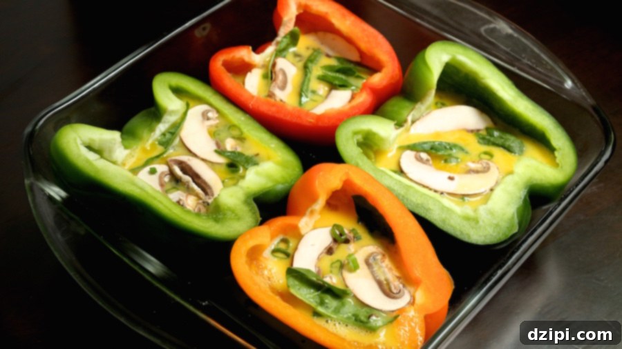 4 bell pepper halves with raw scrambled egg, sliced mushrooms, and spinach in a glass baking pan.