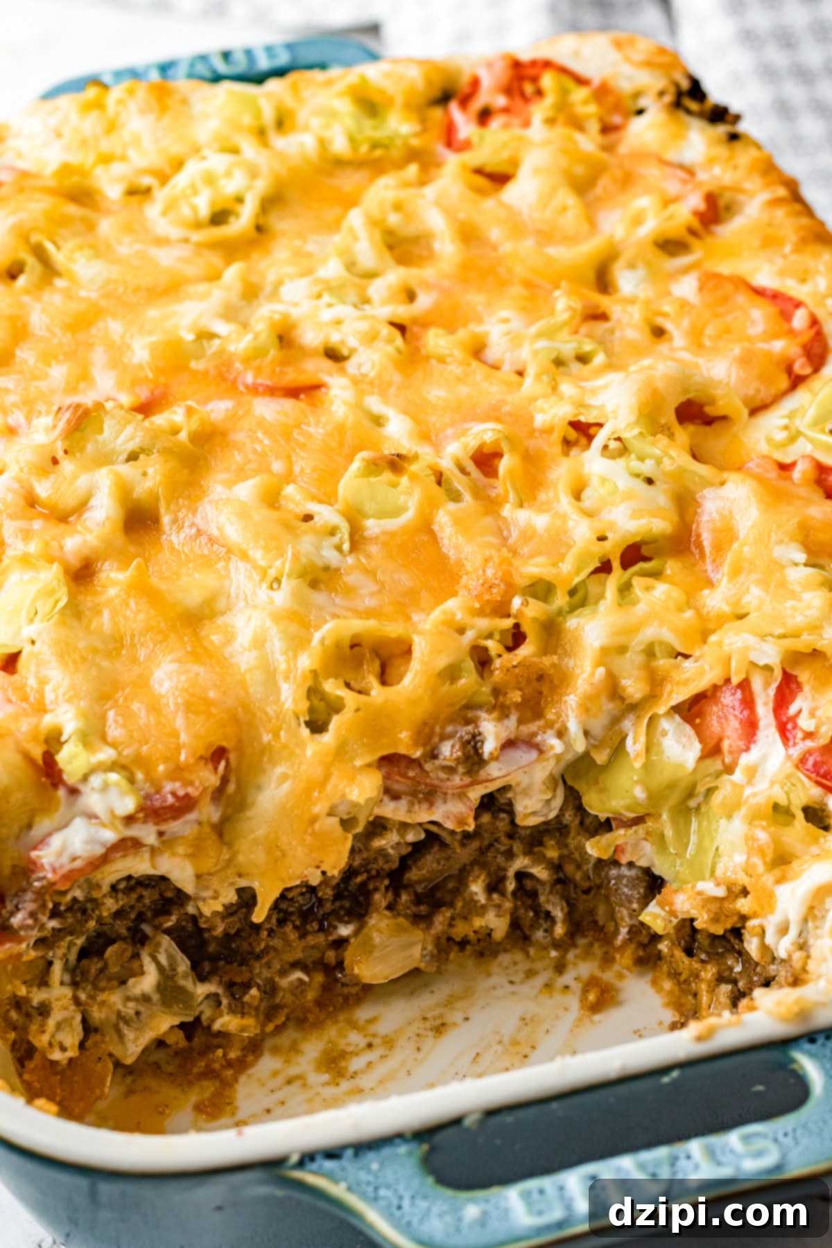 A blue Staub casserole dish filled with John Wayne casserole has a piece cut out to show the ground beef, vegetable, and cheese layers.