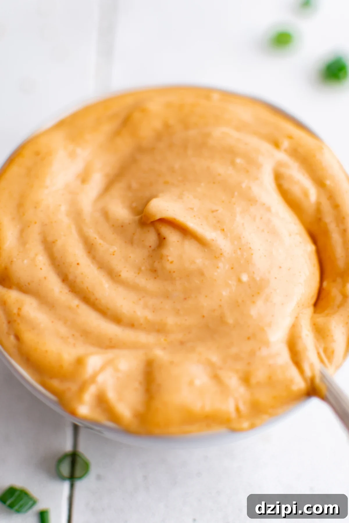 A pristine white bowl brimming with a subtly orange-hued homemade Yum Yum sauce, resting on a clean white tile backdrop. The visual perfectly captures the creamy texture and inviting color of this popular Japanese steakhouse condiment.