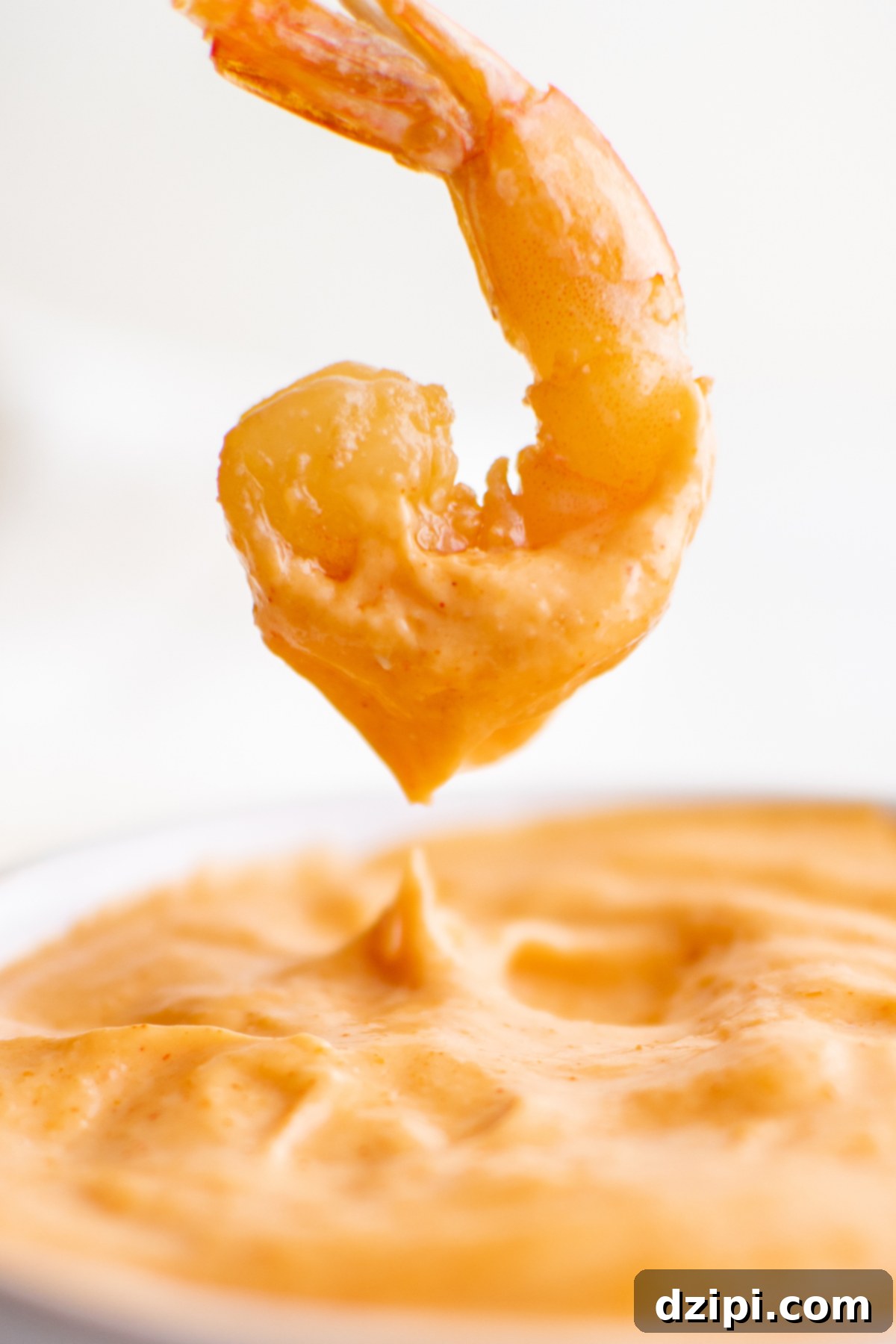 A perfectly cooked hibachi shrimp is carefully dipped into a bowl of creamy, irresistible Yum Yum sauce, showcasing the perfect pairing of flavors.