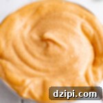 A white bowl filled with a slightly orange 'yum yum sauce' that sits on a white tile background.