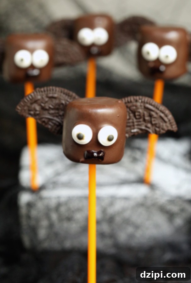 A single chocolate-dipped marshmallow pop designed as a bat, with two Oreo cookie halves for wings and expressive candy eyes, sitting on a flat surface.