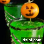 Two bright green Halloween margaritas with black salt rims and mandarin oranges with jack-o-lantern faces drawn on as garnishes sit on a black background.