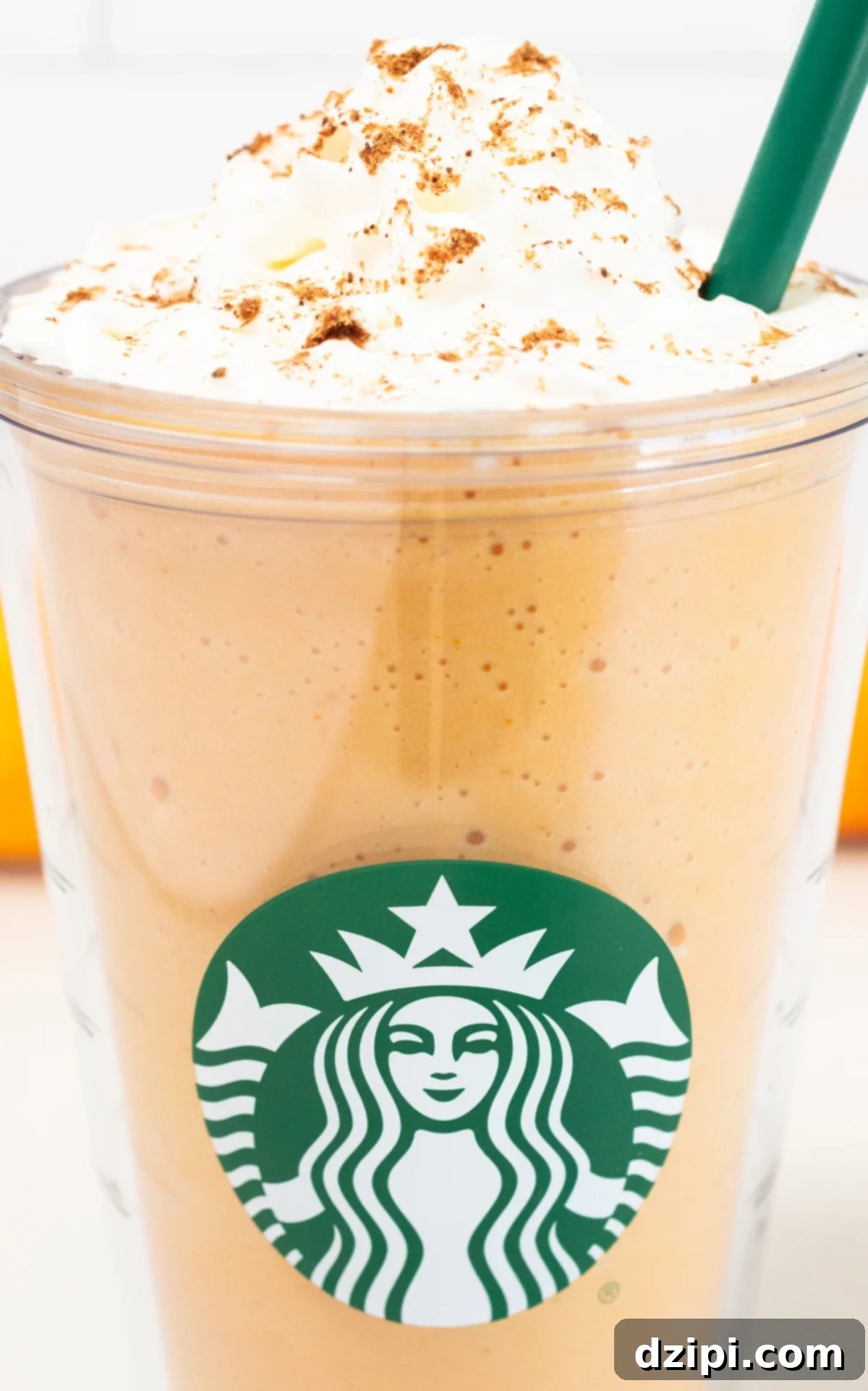 Close up of a starbucks plastic tumbler with a pumpkin spice frappuccino and whipped cream on top.