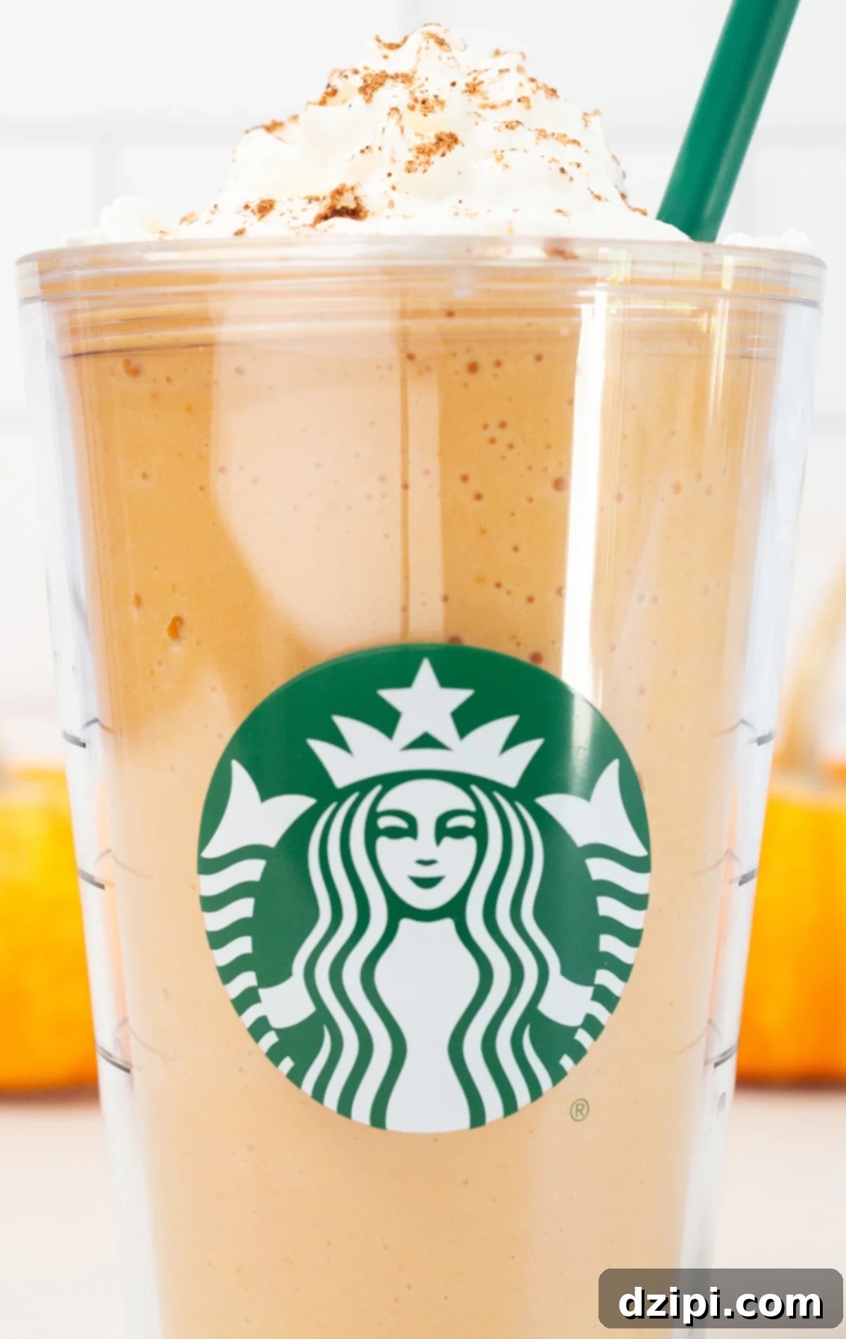 A large plastic tumbler glass with the Starbucks logo is filled with a pumpkin spice frappuccino that's been topped with whipped cream and pumpkin pie spice.