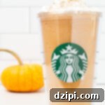 A tall plastic Starbucks tumbler is filled with pumpkin spice frappuccino that's been topped with whipped cream and pumpkin pie spice. A small orange pumpkin is out of focus in the background.