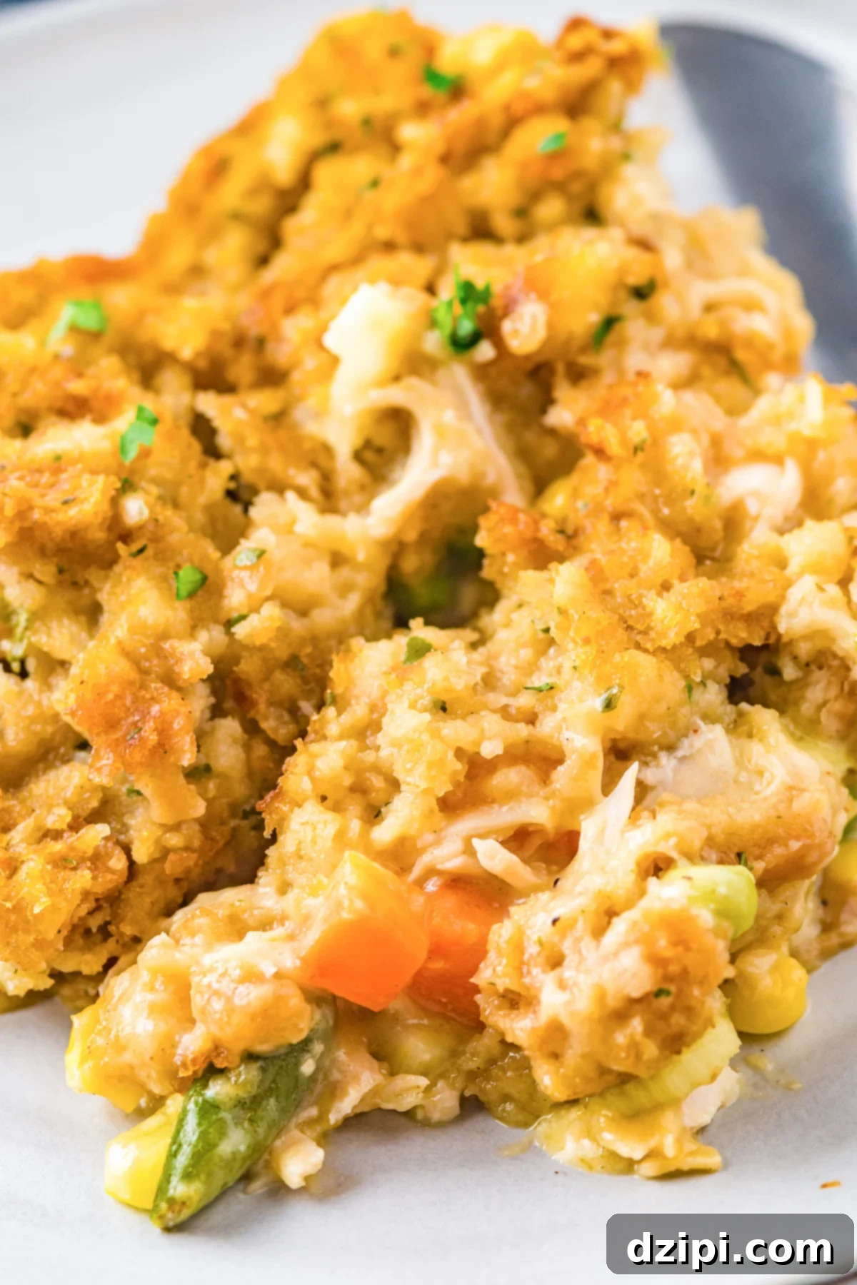 Close up of a bubbling Turkey Stuffing Casserole, showcasing golden-brown stuffing topping and tender turkey with chopped vegetables nestled underneath.