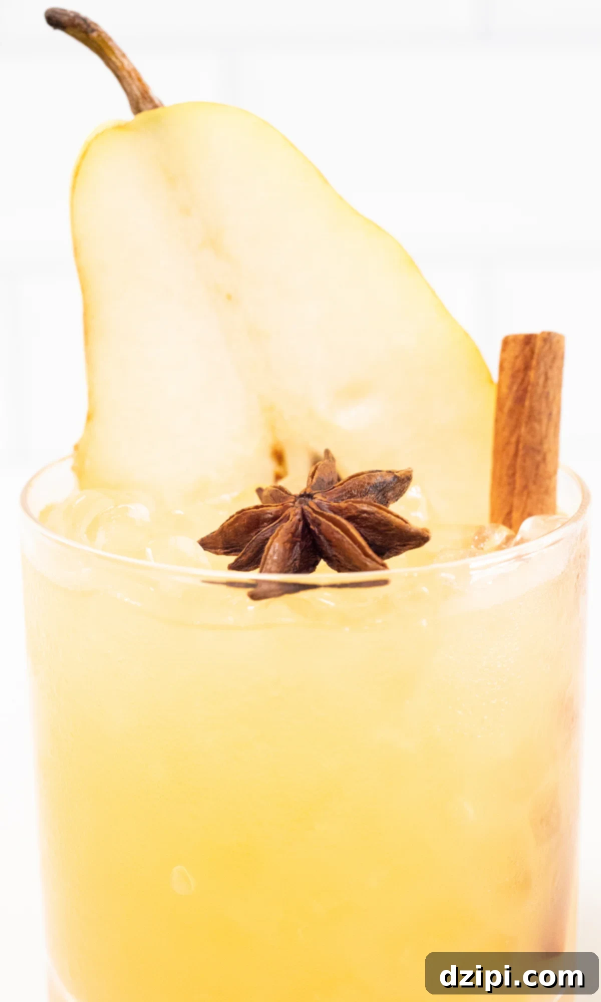 Close-up shot of a Thanksgiving cocktail served in a lowball glass, beautifully garnished with a star anise, a cinnamon stick, and a fresh pear slice. The focus highlights the intricate details and inviting colors of the drink.