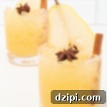 Two lowball glasses on a white background. They are filled with a yellow Thanksgiving cocktail that's garnished with a pear slice, star anise, and a cinnamon stick.