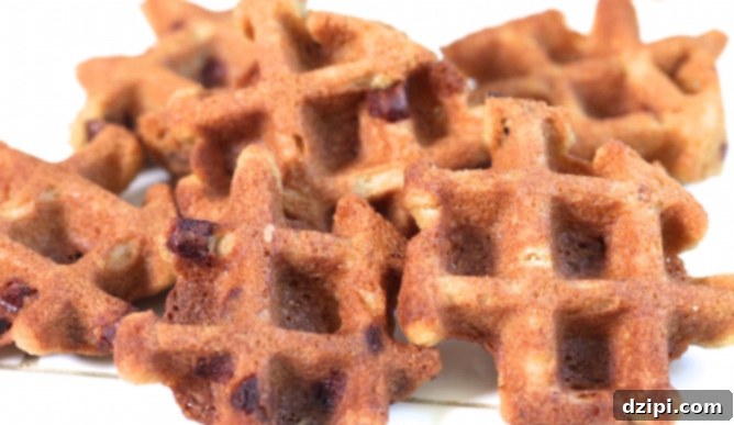 A delectable stack of golden-brown chocolate chip cookies, freshly baked in a waffle maker, resting on a clean white surface. Each cookie features distinct waffle grooves and visible melted chocolate chips, hinting at a warm, soft interior.