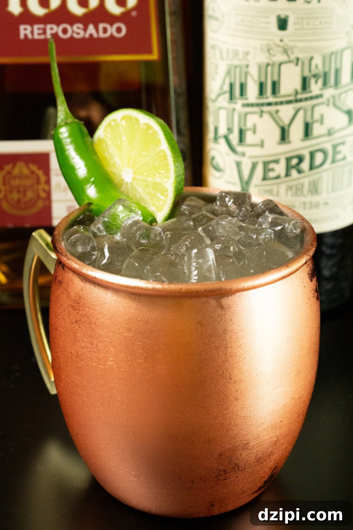 A glistening copper mug brimming with pebble ice and a vibrant Mexican Mule cocktail, positioned enticingly in front of a bottle of premium tequila and a dark chile liqueur.