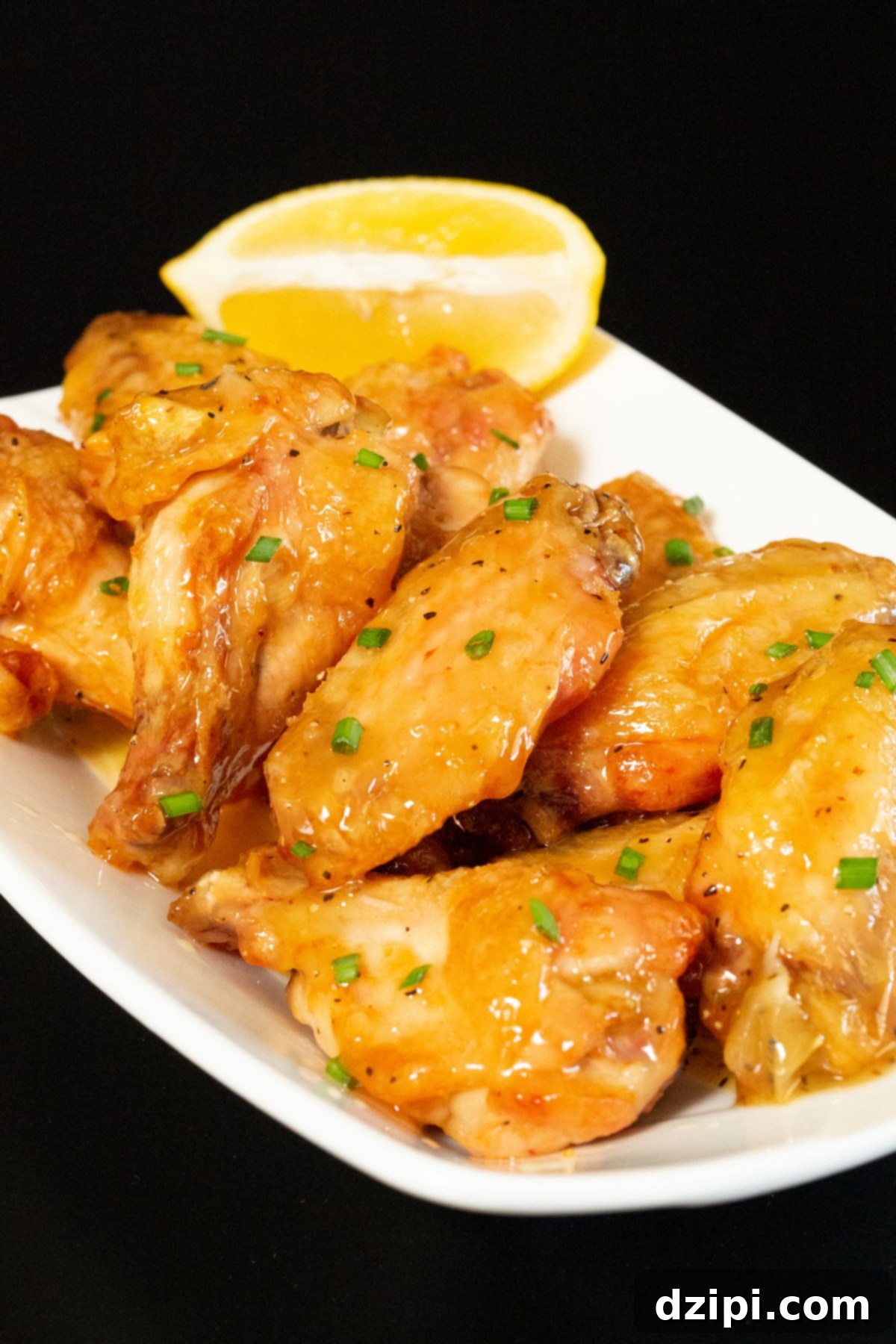 Golden brown crispy chicken wings glistening with honey lemon pepper glaze, served on a dark background.
