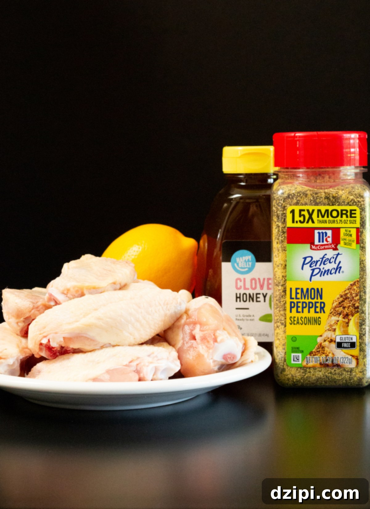 Individual ingredients for honey lemon pepper wings, including chicken, lemon, honey, and seasoning, neatly arranged on a black background.
