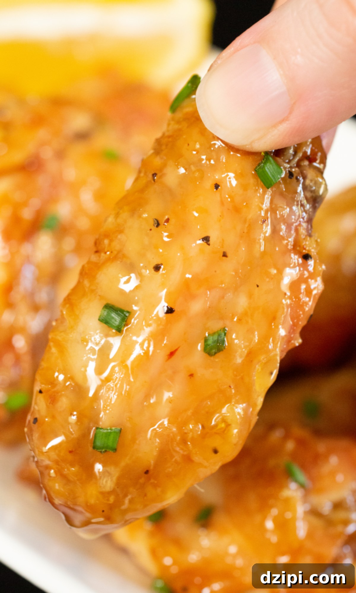 A single honey lemon pepper wing held up against a blurred background of a basket filled with more wings.