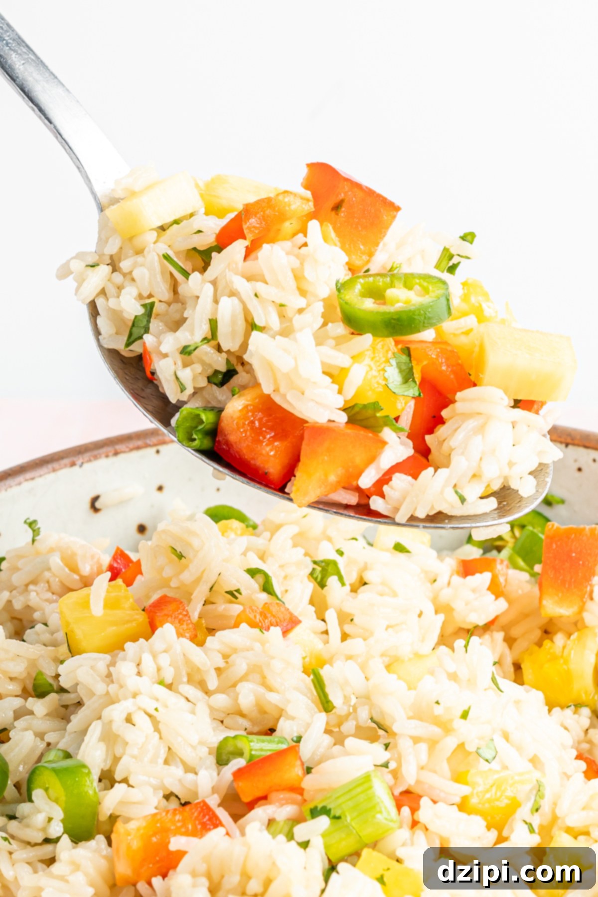 A spoonful of fluffy Instant Pot coconut rice being lifted from a bowl filled with the tropical rice and its colorful additions.