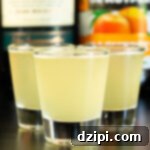 Three shot glasses filled with green tea shots in front of Jameson and peach schnapps bottles.