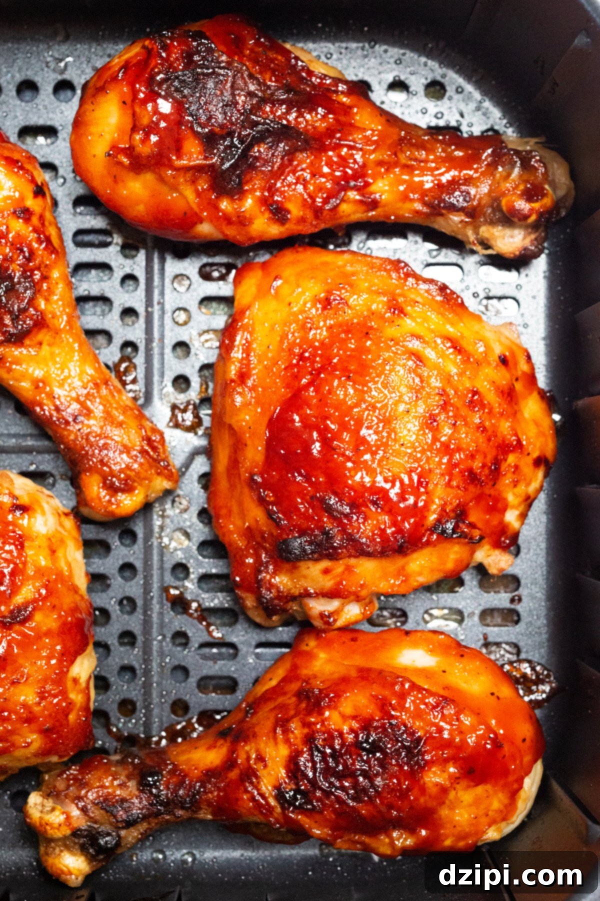 A basket full of perfectly cooked BBQ chicken legs and thighs from an air fryer, showcasing the crispy skin and rich sauce.