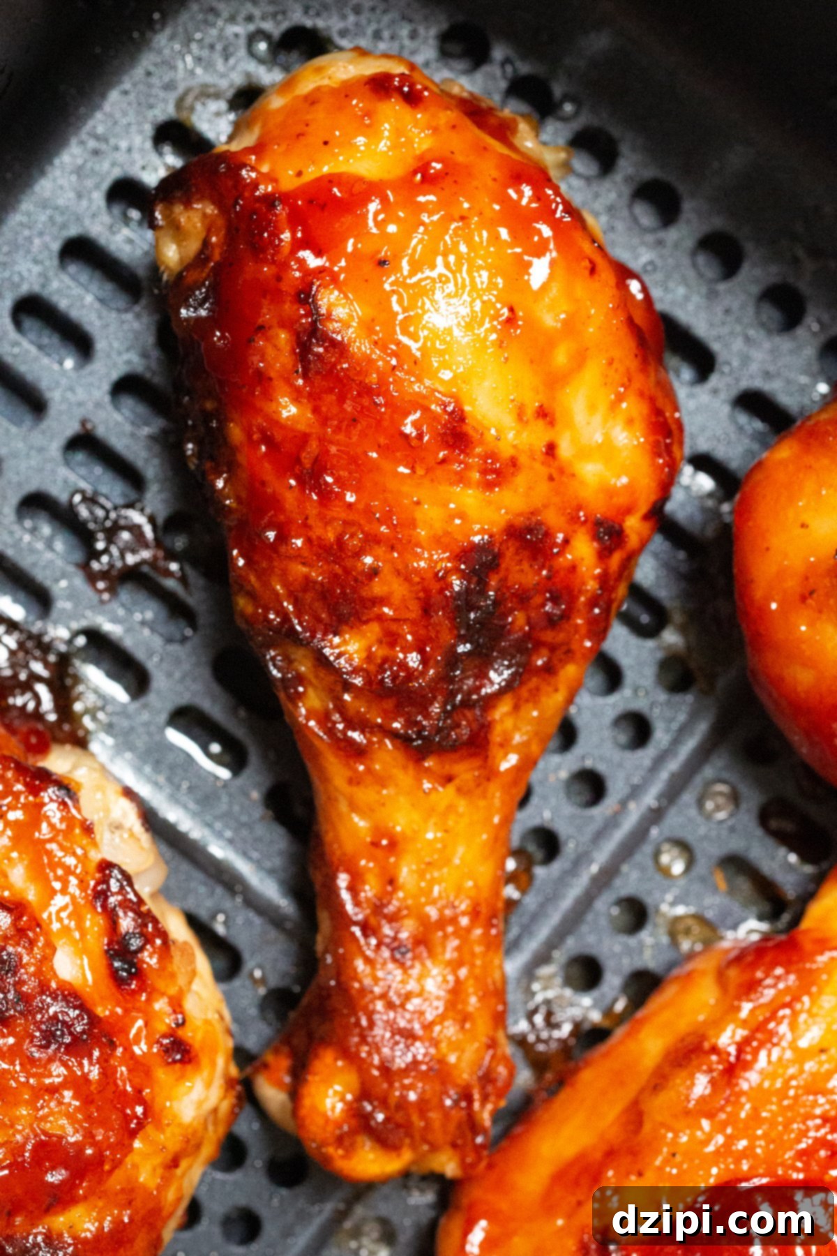 A single, perfectly cooked BBQ chicken drumstick resting in an air fryer basket, showing off its glazed skin.