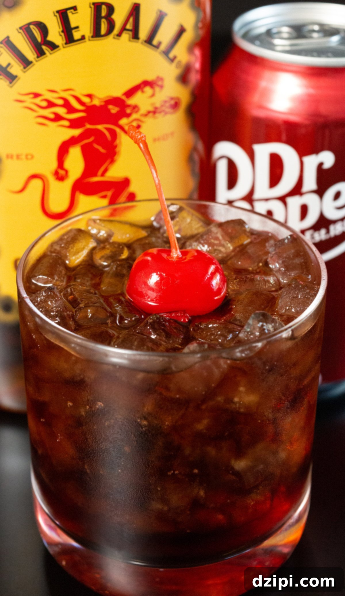 A Fireball Dr. Pepper cocktail in a rocks glass with a cherry on top, ready to be enjoyed.