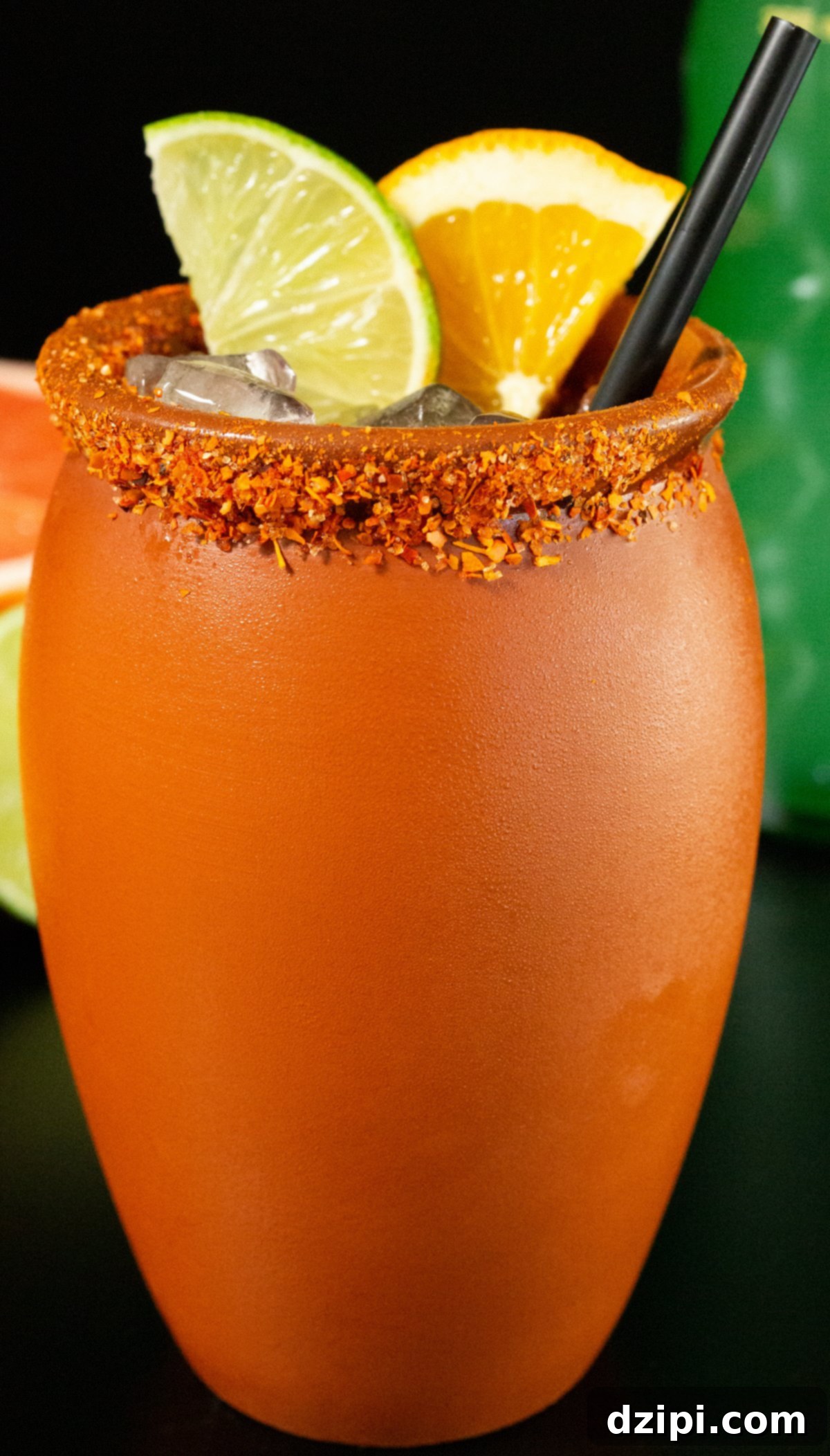 A traditional clay glass with a chile salt rim, adorned with lime and orange slices, featuring a black straw – a vibrant Cantarito.