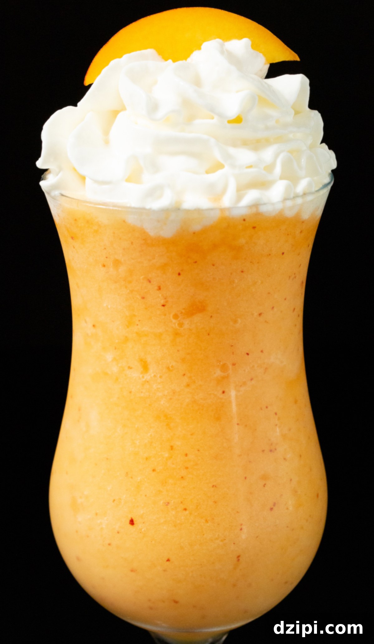 A hurricane glass filled with a luscious frozen Peach Daiquiri, garnished with a fresh peach slice and a dollop of whipped cream.
