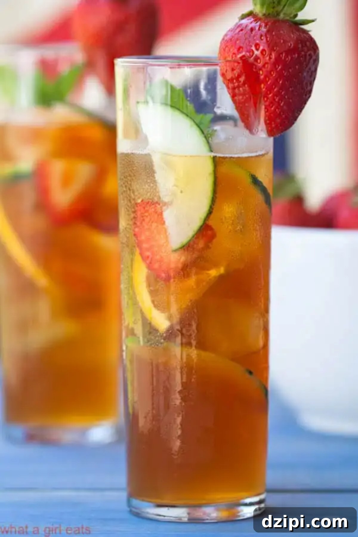 A tall glass brimming with a Pimm's Cup cocktail, packed with an array of fresh sliced fruit and vegetables, like cucumber and strawberries.