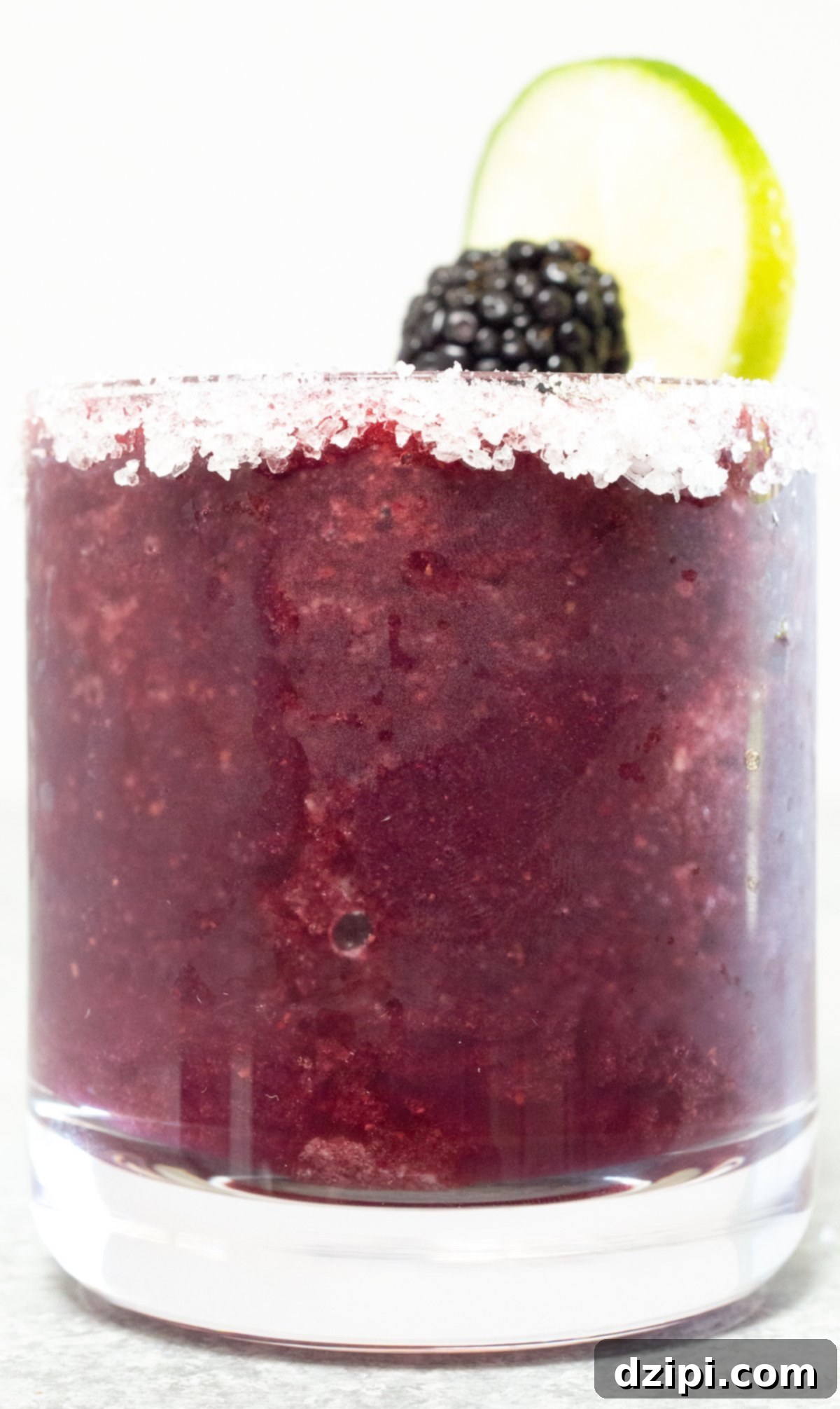 A glass filled with a vibrant purple Blackberry Margarita, showcasing its rich color against a white background.