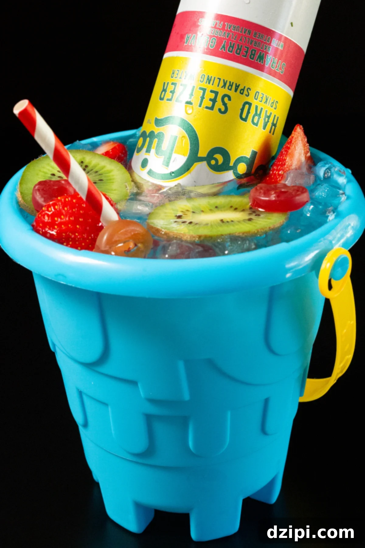 A playful blue sand bucket filled with a colorful cocktail, adorned with sliced strawberries, kiwis, and gummy lifesavers – the ultimate vacation drink.