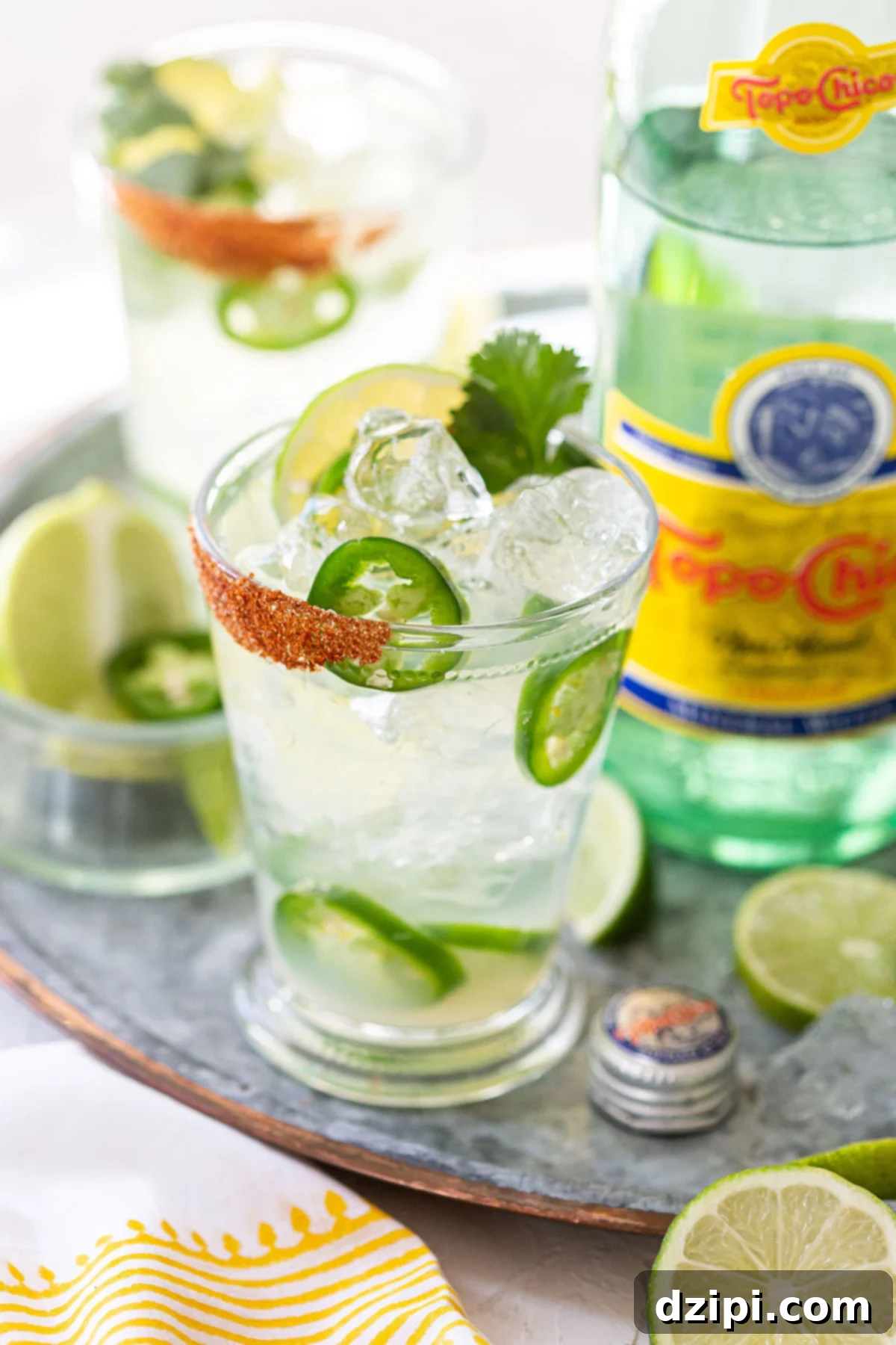 A pint glass filled with Spicy Ranch Water and thin jalapeño slices, sitting in front of a bottle of Topo Chico, highlighting its refreshing kick.