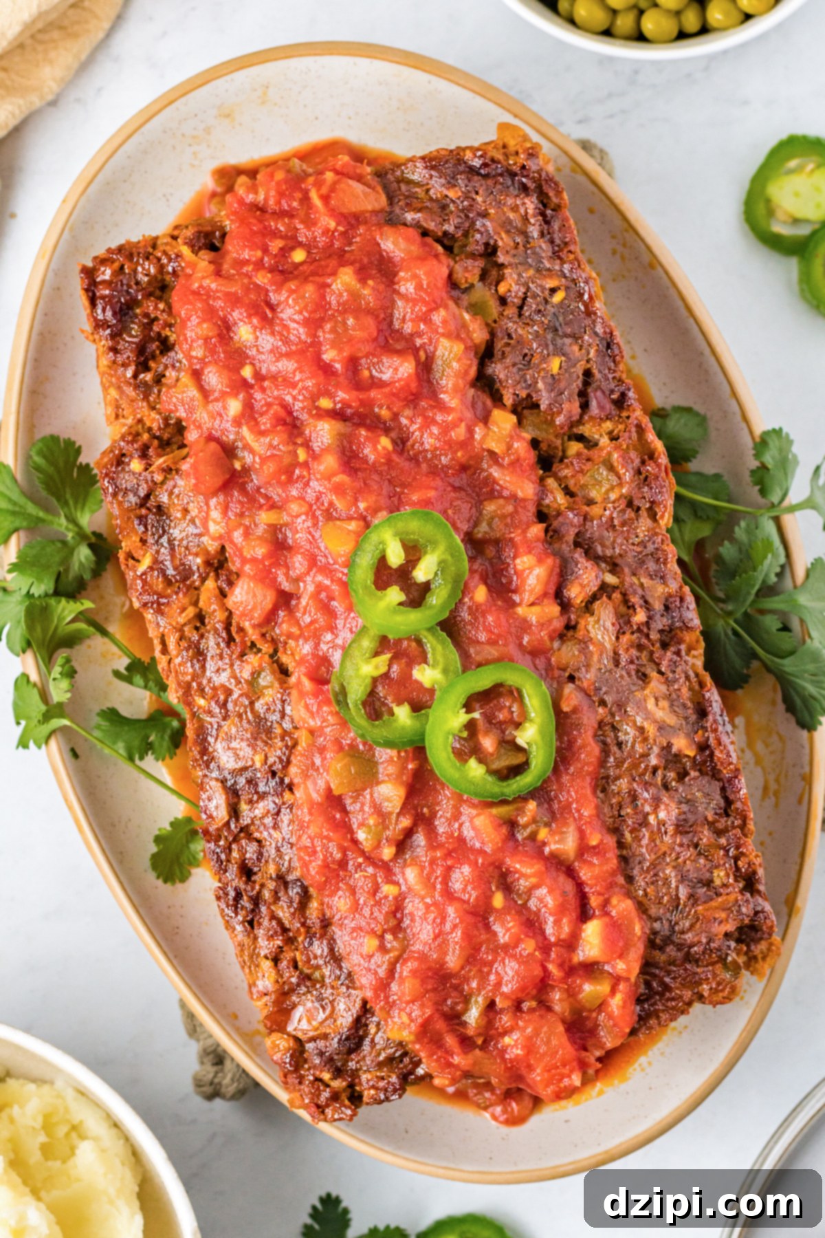 Fiesta Meatloaf 2 A Mexican meatloaf topped with salsa and sliced jalapeño on a serving platter, ready to be enjoyed.