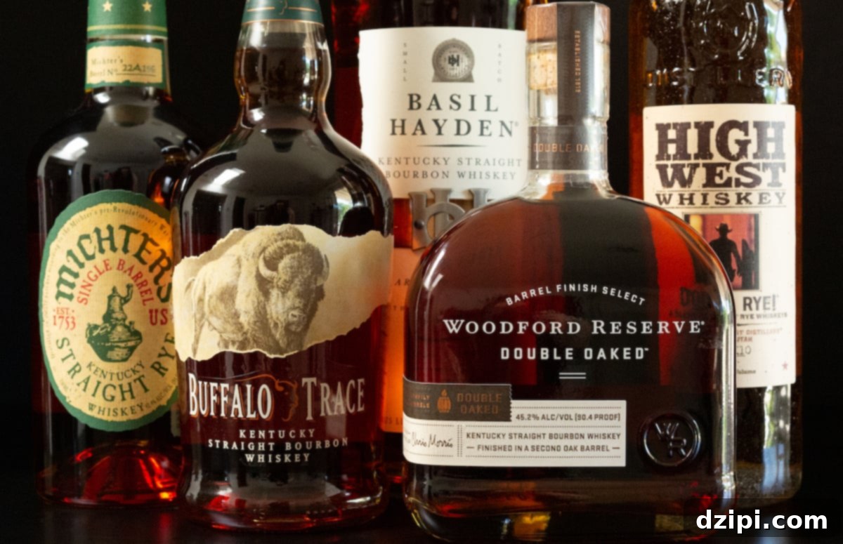 Five different bottles of whiskey are on a black background, with an Old Fashioned cocktail in the foreground.