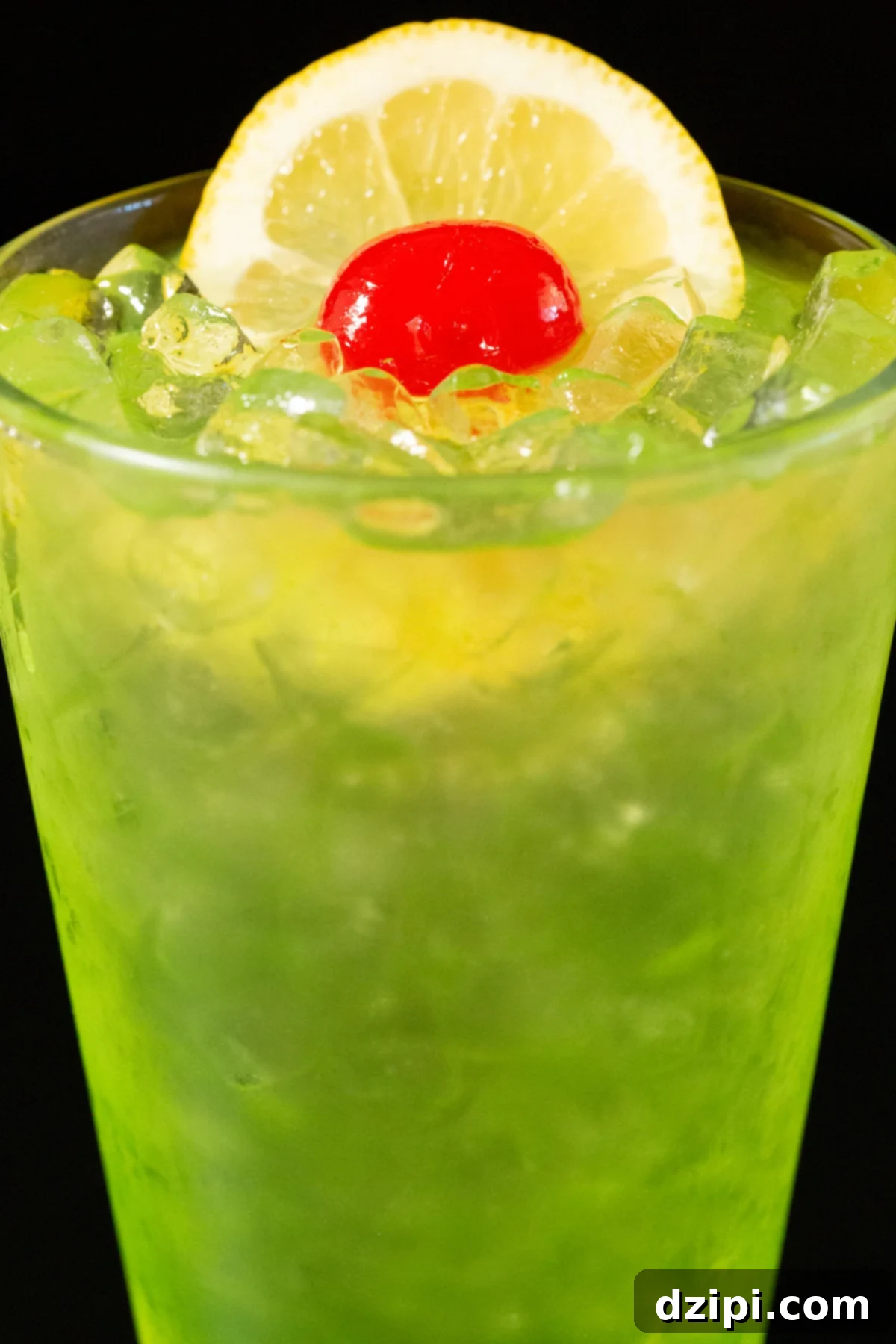 Close up of a pint glass filled with a neon green Tokyo Iced Tea Cocktail that's topped with a lime wheel and maraschino cherry.