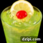 A pint glass filled with a neon green Tokyo Iced Tea cocktail garnished with a lemon wheel and maraschino cherry.