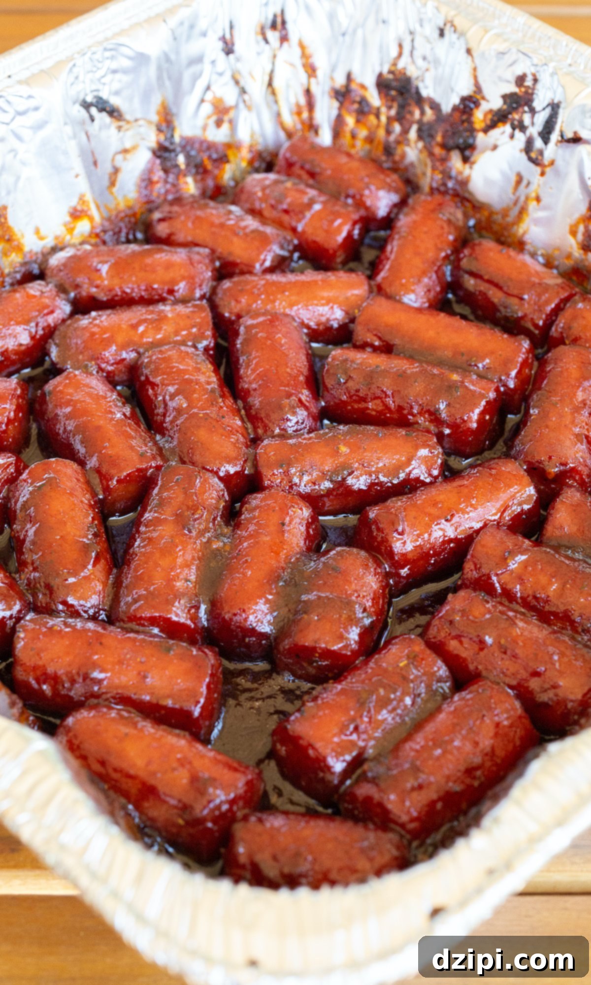 A disposable foil pan filled with hot dog burnt ends covered in thick sauce.