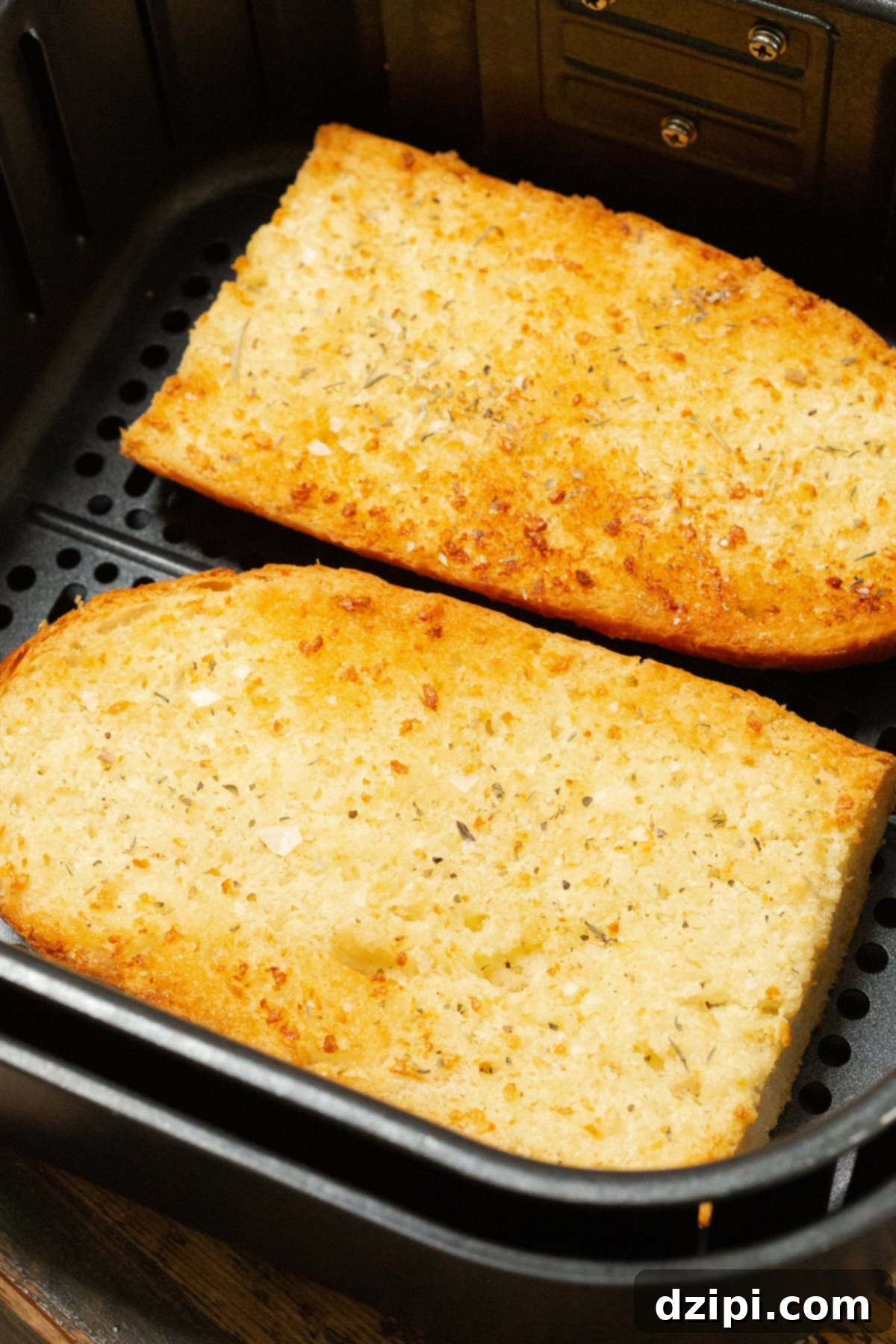 Two halves of a French loaf, generously spread with garlic butter, placed in an air fryer basket before cooking.