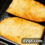 Two pieces of garlic bread French loaf in the air fryer basket.