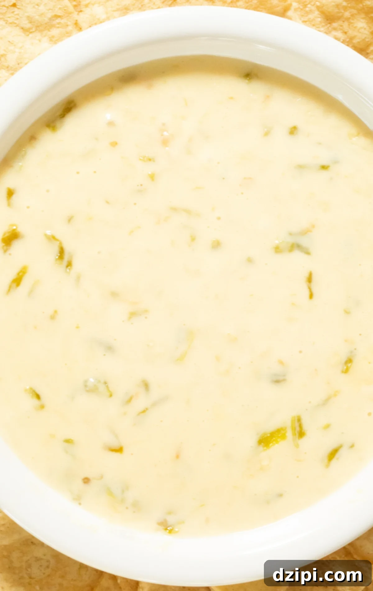 A white bowl filled with a light colored hatch queso that has visible chopped hatch green chiles throughout, ready for dipping.