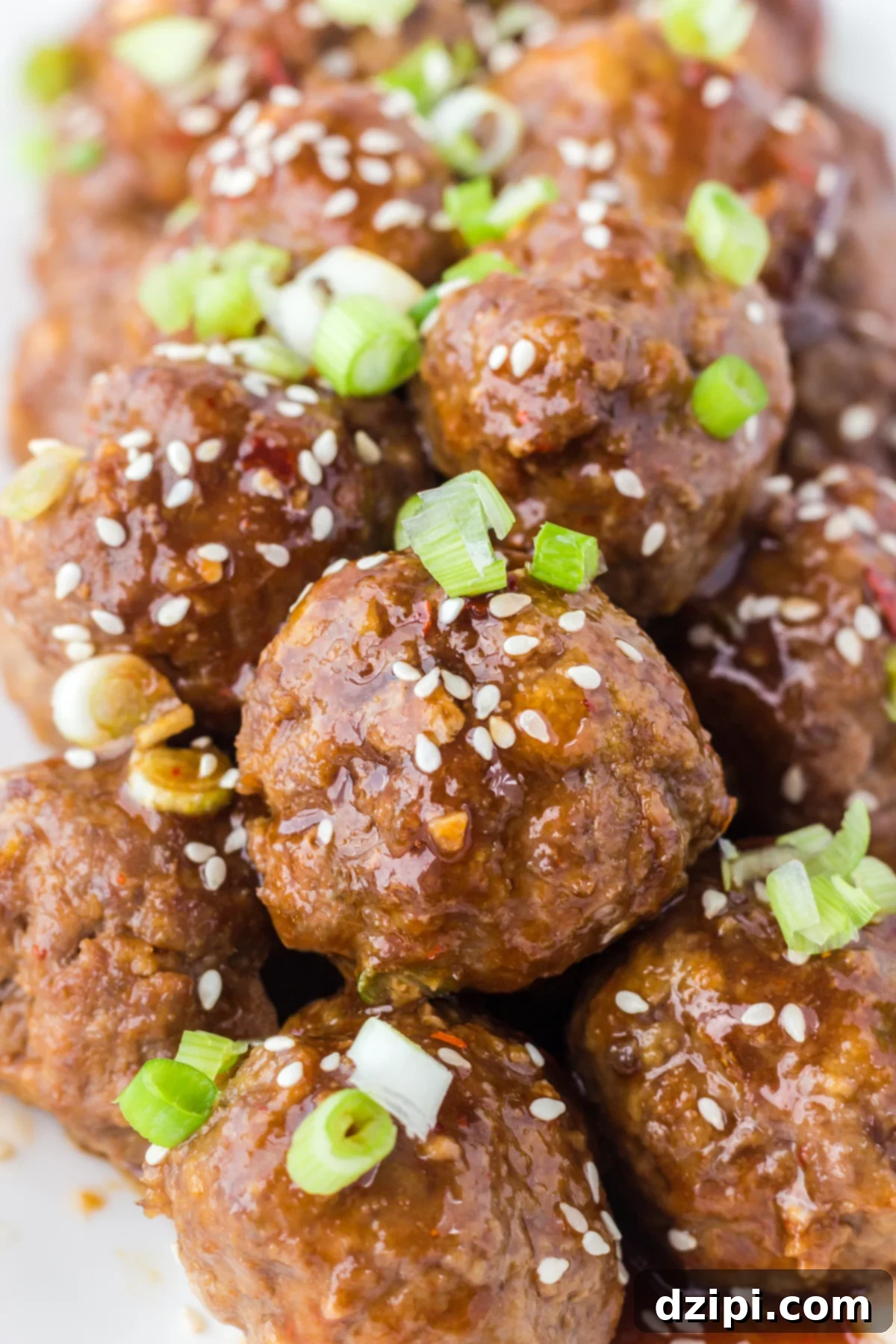 Dozens of Asian meatballs covered in brown sauce, sesame seeds, and sliced green onions.