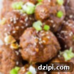 Dozens of Asian meatballs covered in brown sauce, sesame seeds, and sliced green onions.