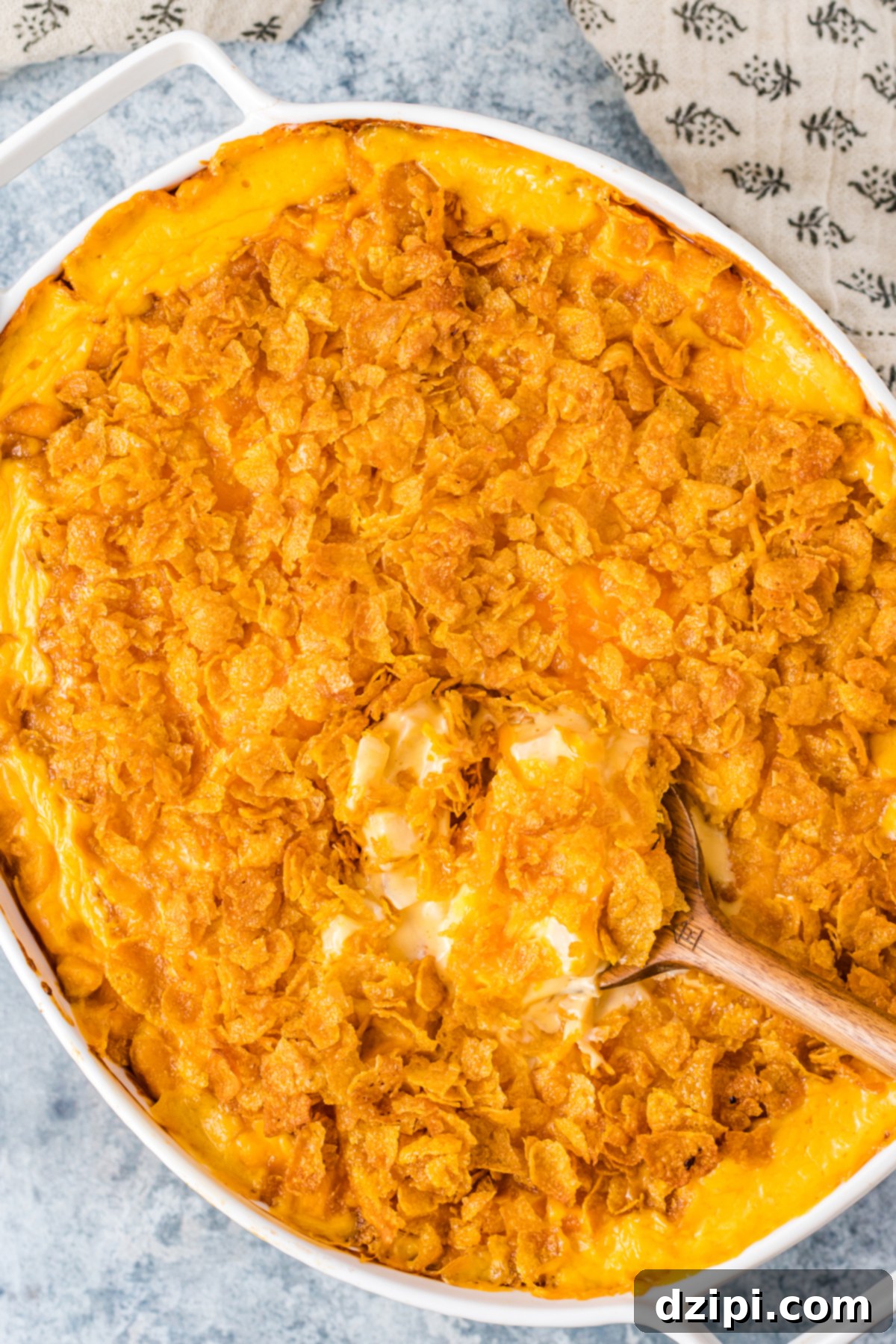 Overhead view of white oval baking dish filled with orange, cheesy funeral potatoes topped with cornflakes.